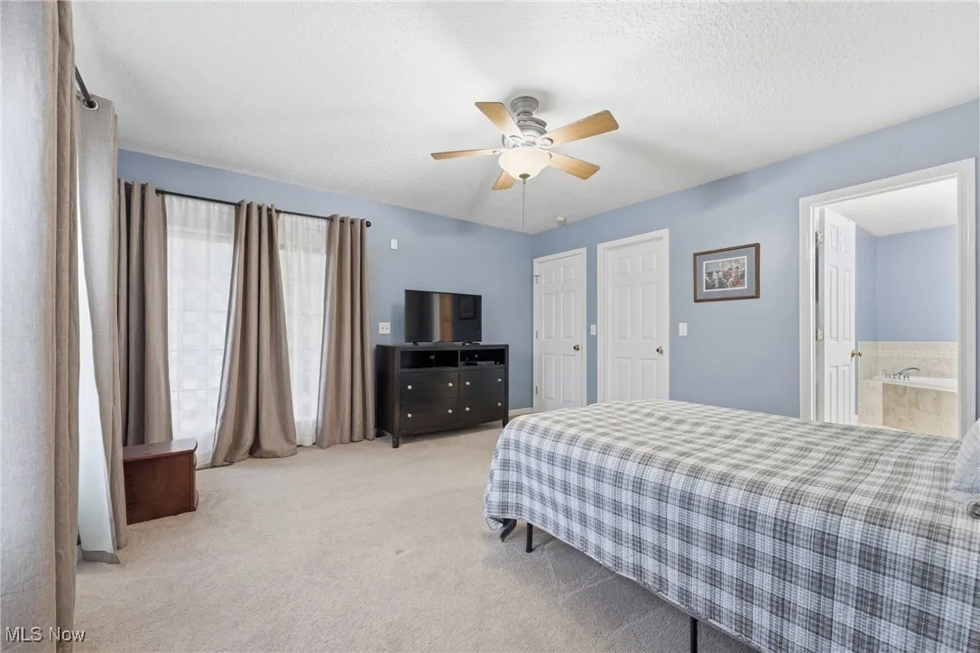 Carpeted bedroom featuring a ceiling fan, a textured ceiling, ensuite bathroom, and a closet