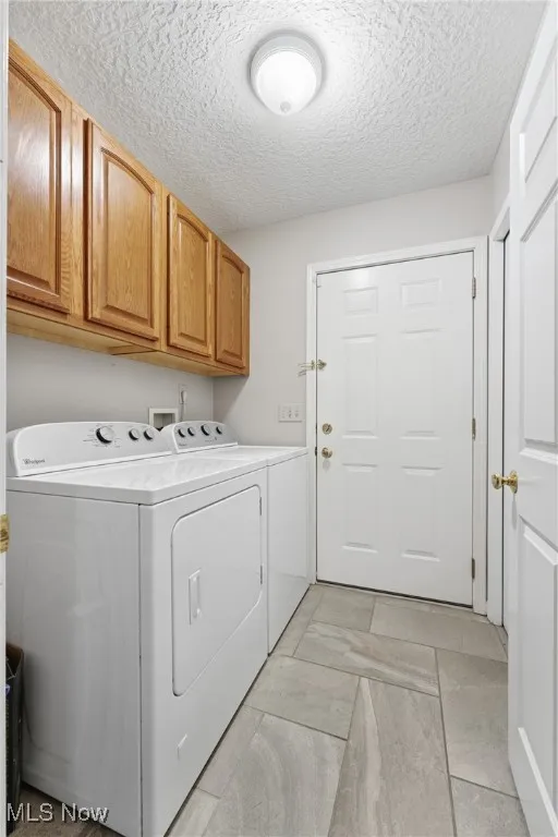 Laundry area featuring a textured ceiling, cabinet space, and washing machine and dryer