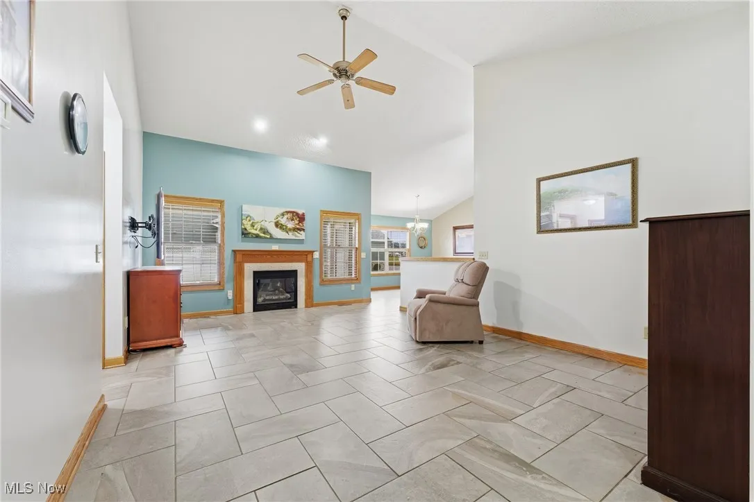 Sitting room featuring a glass covered fireplace, a chandelier, a ceiling fan, and high vaulted ceiling