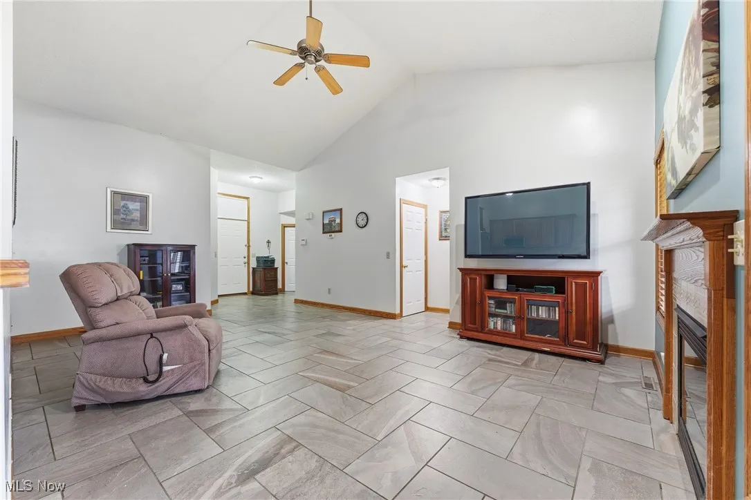 Living area with high vaulted ceiling, ceiling fan, and a tile fireplace