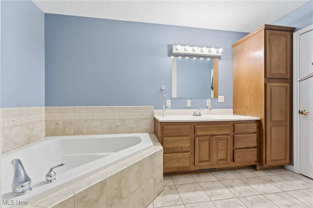 Full bathroom featuring vanity, a garden tub, a textured ceiling, and light tile patterned floors