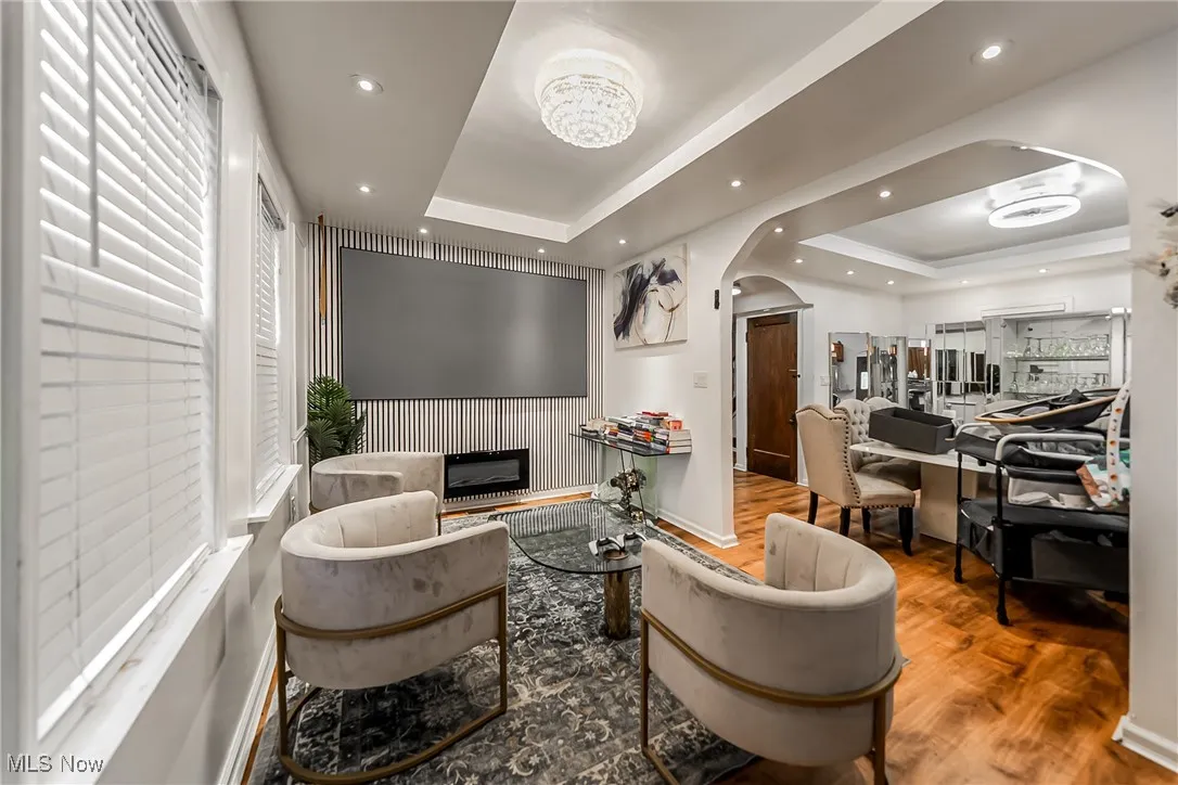 Living room with arched walkways, a raised ceiling, wood finished floors, an accent wall, and recessed lighting
