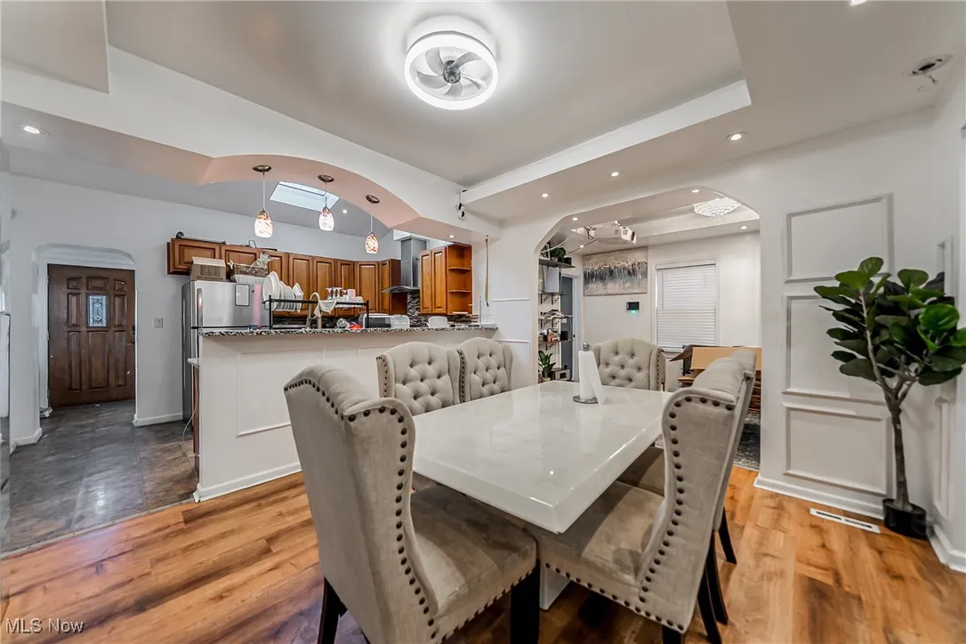 Dining room with arched walkways, recessed lighting, dark wood-style floors, and a raised ceiling