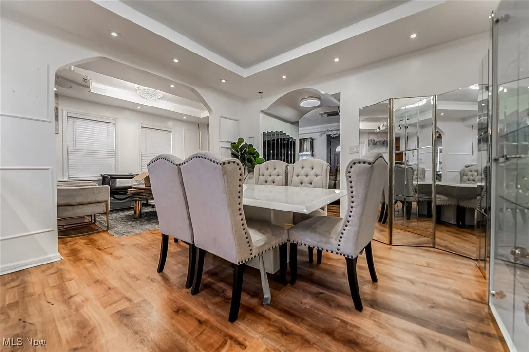 Dining space with a raised ceiling, arched walkways, light wood finished floors, and recessed lighting