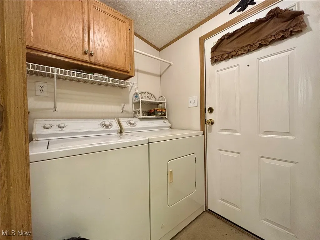 Washroom with ornamental molding, a textured ceiling, cabinet space, and washer and clothes dryer