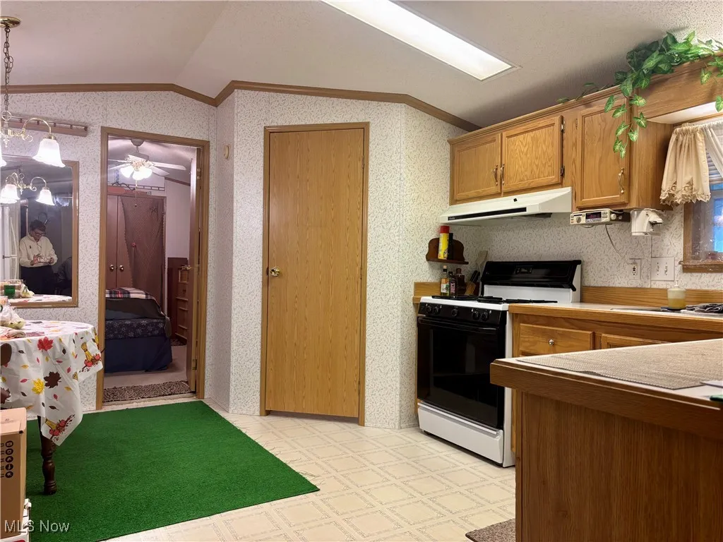 Kitchen featuring lofted ceiling, gas range oven, ornamental molding, wallpapered walls, and under cabinet range hood