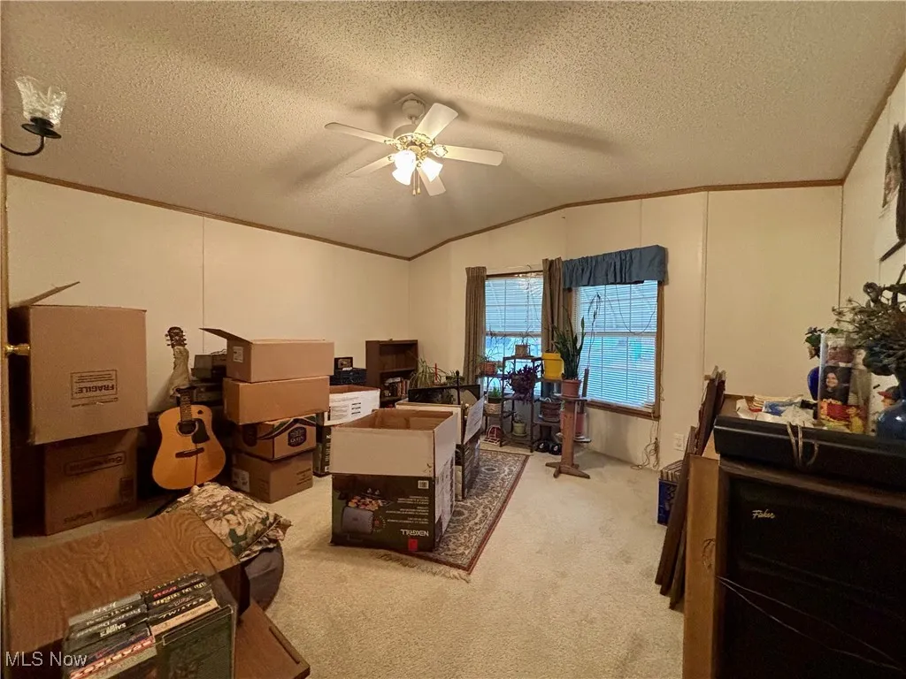 Home office featuring ornamental molding, vaulted ceiling, a textured ceiling, light carpet, and a ceiling fan