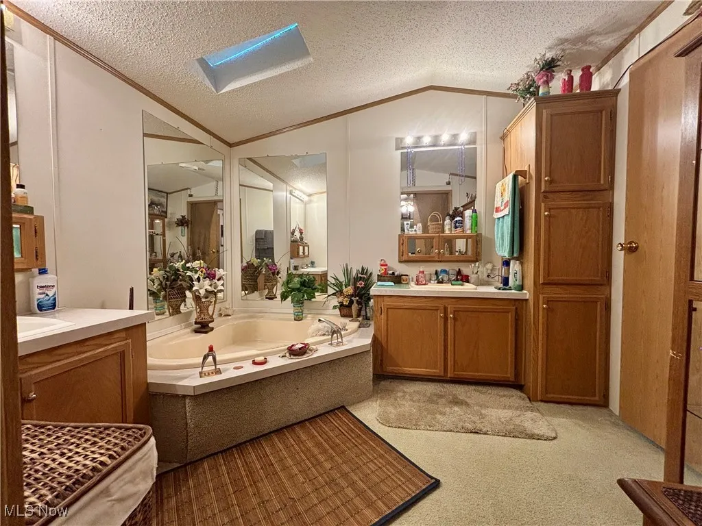 Full bathroom featuring vaulted ceiling, ornamental molding, two vanities, a bath, and a textured ceiling