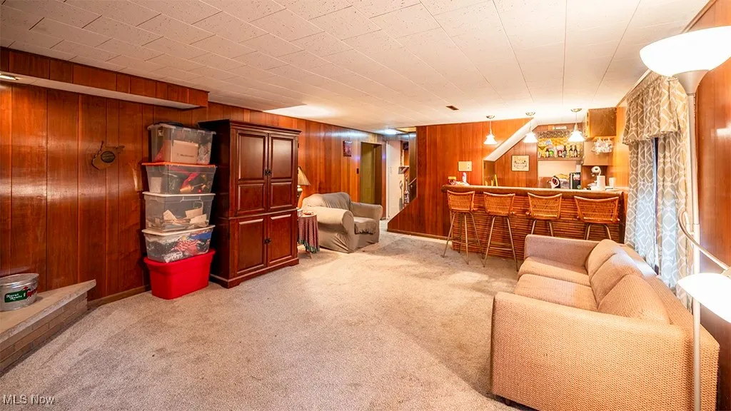 Living area featuring light colored carpet, wooden walls, and bar area