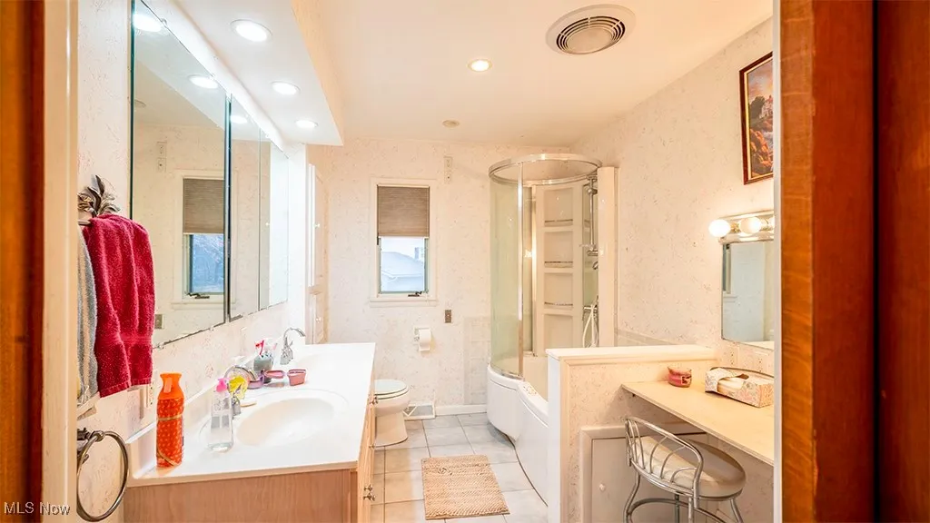 Bathroom with double vanity, light tile patterned floors, enclosed tub / shower combo, wallpapered walls, and recessed lighting