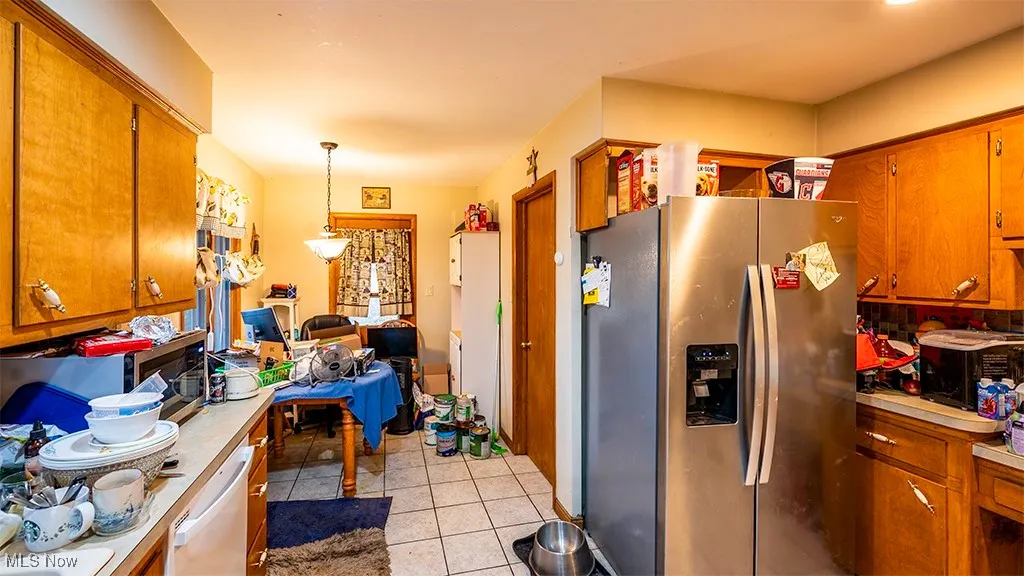 Kitchen with brown cabinets, stainless steel appliances, light countertops, light tile patterned floors, and decorative light fixtures