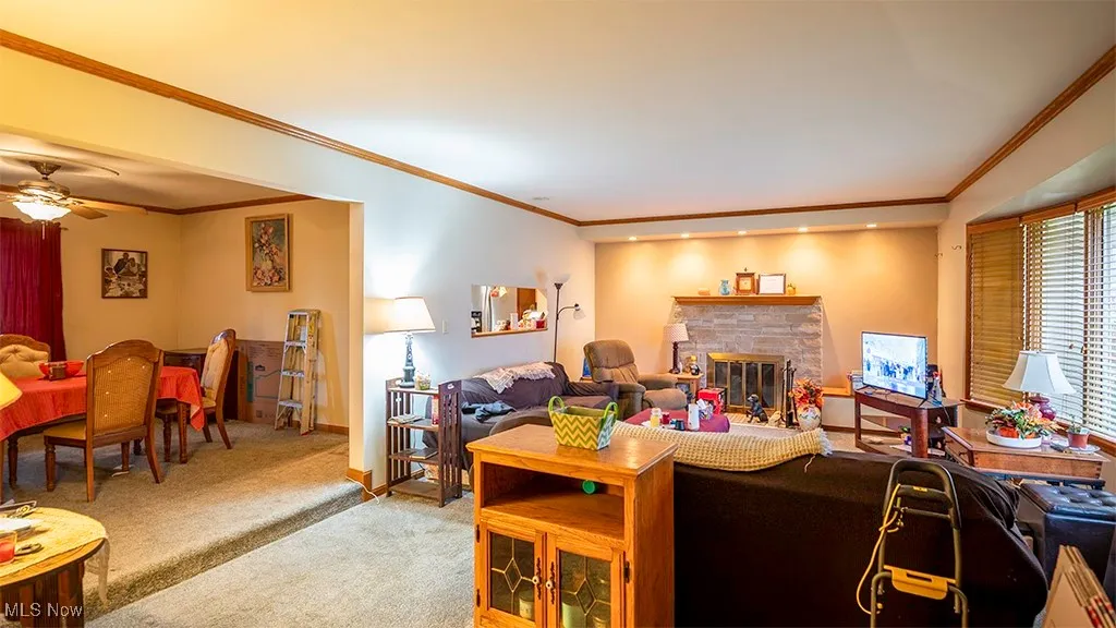 Carpeted living area with crown molding, a fireplace, and ceiling fan