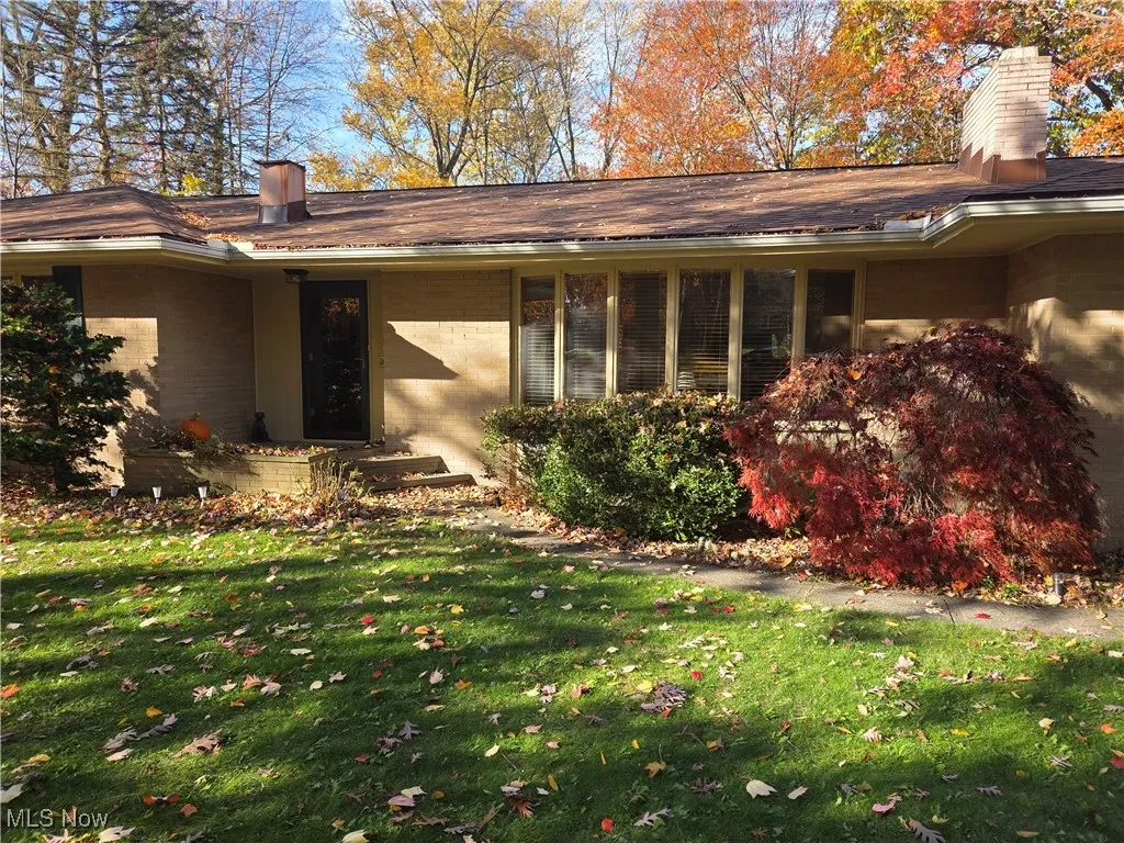 View of side of home with brick siding, a lawn, a chimney, and a porch