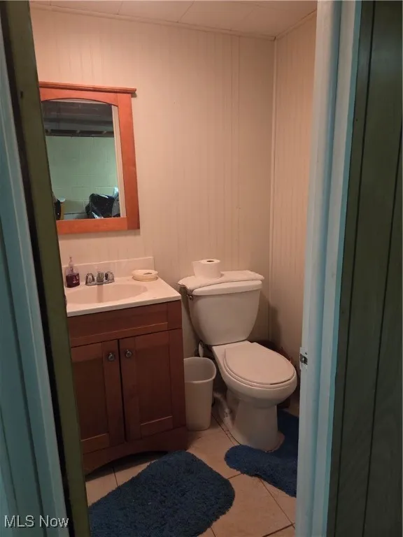 Basement Half bathroom featuring light tile patterned flooring, vanity, and wooden walls
