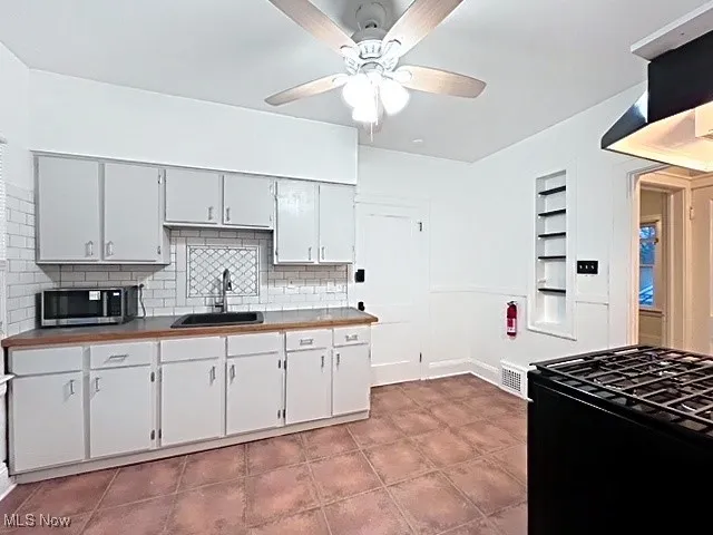 Kitchen featuring built in features, black range with gas stovetop, stainless steel microwave, ceiling fan, and white cabinets