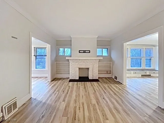 Unfurnished living room featuring light wood-style floors, a fireplace, and crown molding
