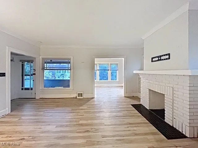 Unfurnished living room featuring light wood-style flooring, ornamental molding, and a brick fireplace