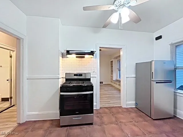 Kitchen featuring appliances with stainless steel finishes, a ceiling fan, extractor fan, and dark tile patterned flooring