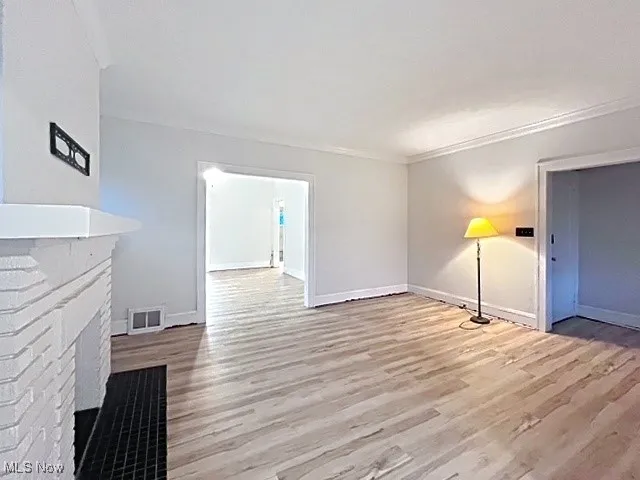 Unfurnished living room featuring light wood-style floors, a multi sided fireplace, and crown molding
