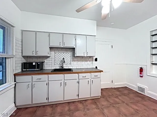 Kitchen with stainless steel microwave, tasteful backsplash, ceiling fan, and white cabinetry