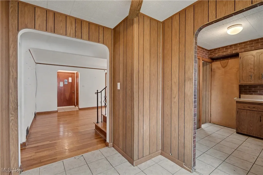Hallway with arched walkways, light tile patterned floors, wooden walls, and stairs