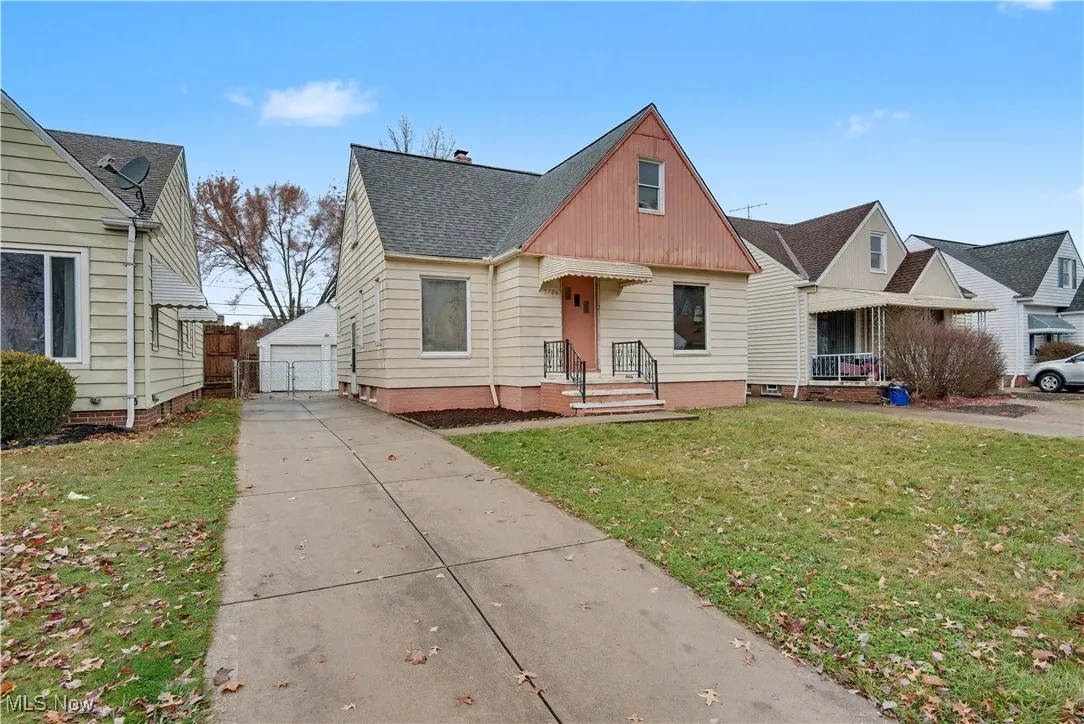 Bungalow-style house featuring a front lawn, a detached garage, a gate, and a shingled roof