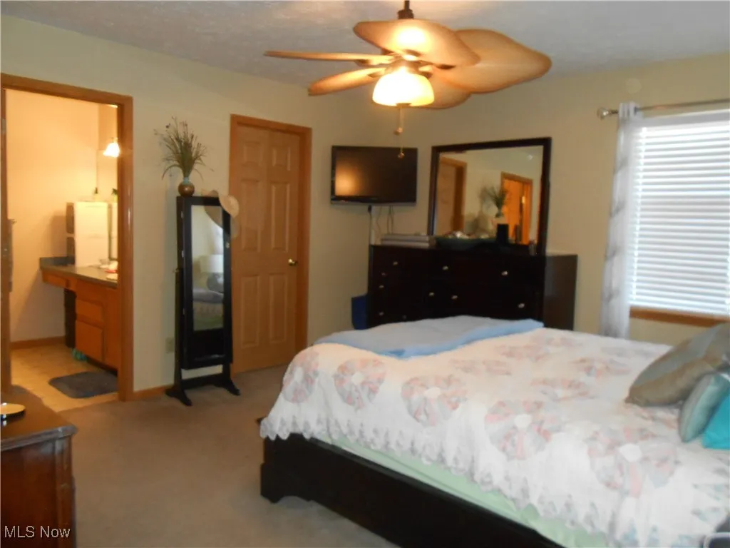 Bedroom with light carpet, connected bathroom, ceiling fan, and a textured ceiling