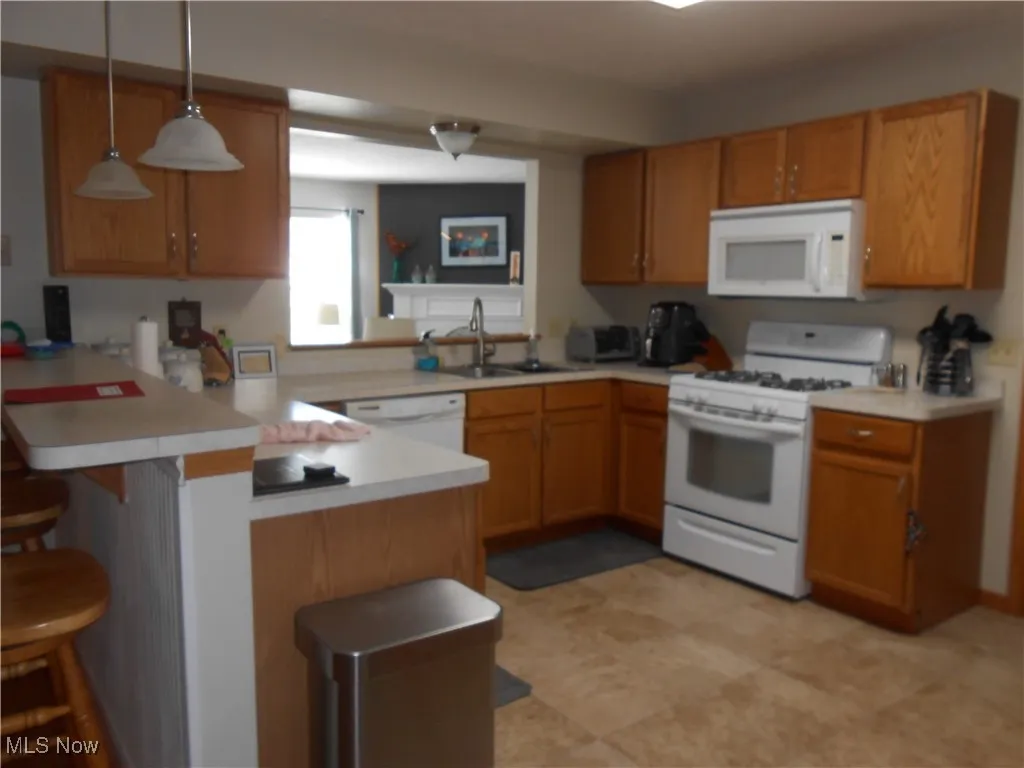 Kitchen featuring white appliances, light countertops, a breakfast bar, decorative light fixtures, and a peninsula