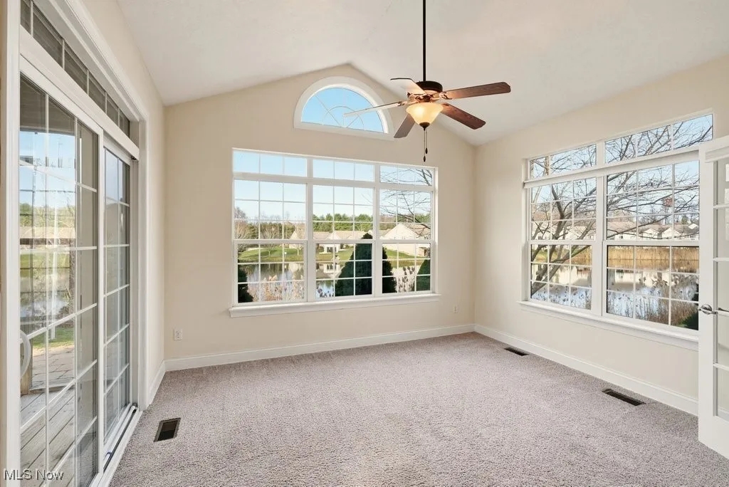 Sun room with vaulted ceiling, light colored carpet, plenty of natural light, and a ceiling fan