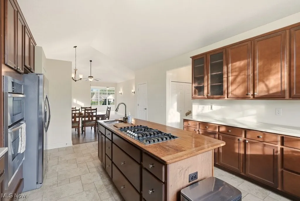 Kitchen featuring an island with sink, vaulted ceiling, hanging light fixtures, stainless steel appliances, and glass insert cabinets