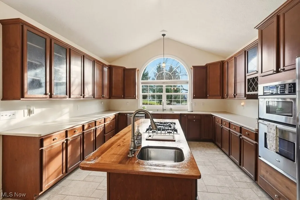 Kitchen featuring vaulted ceiling, stainless steel appliances, wood counters, decorative light fixtures, and a kitchen island with sink