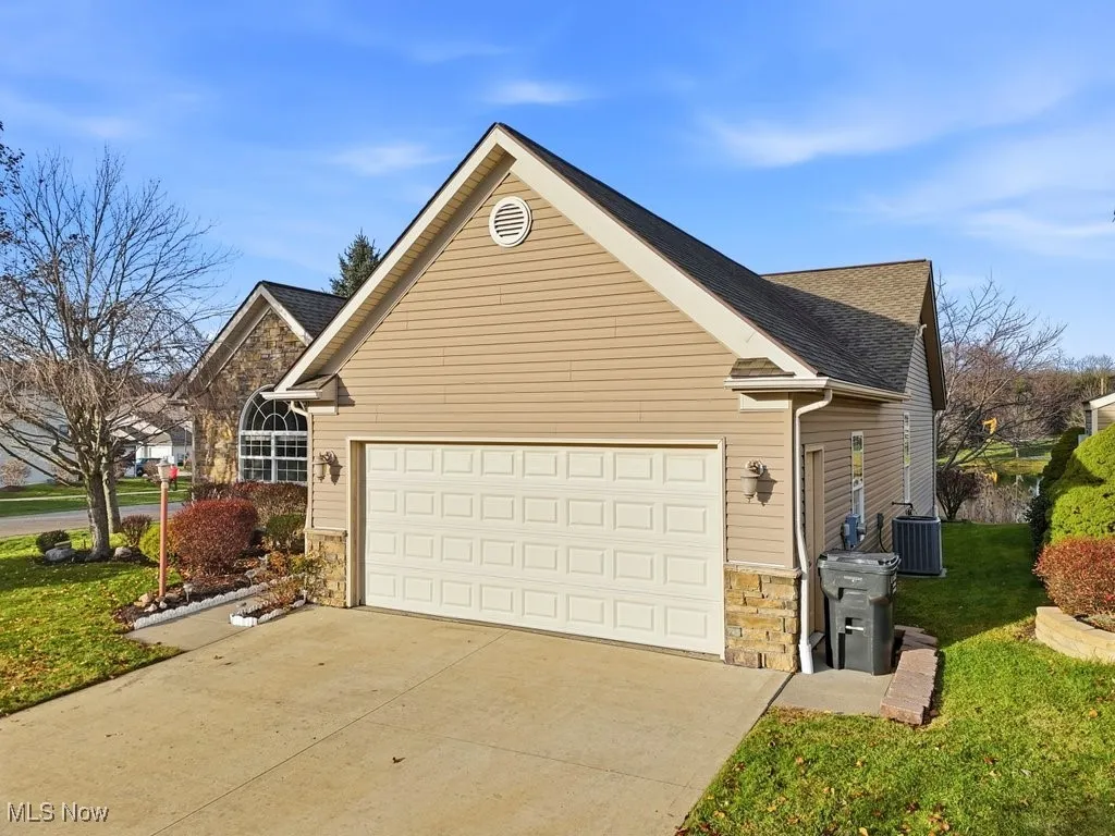 View of front facade with stone siding, concrete driveway, an attached garage, and a front lawn