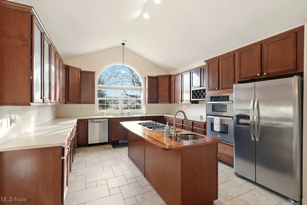 Kitchen featuring appliances with stainless steel finishes, hanging light fixtures, vaulted ceiling, a center island with sink, and butcher block counters