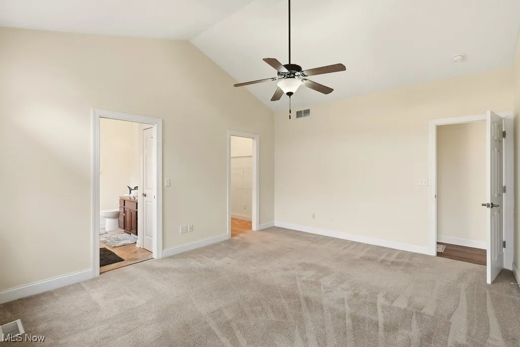 Primary bedroom featuring connected bathroom, light carpet, high vaulted ceiling, and ceiling fan