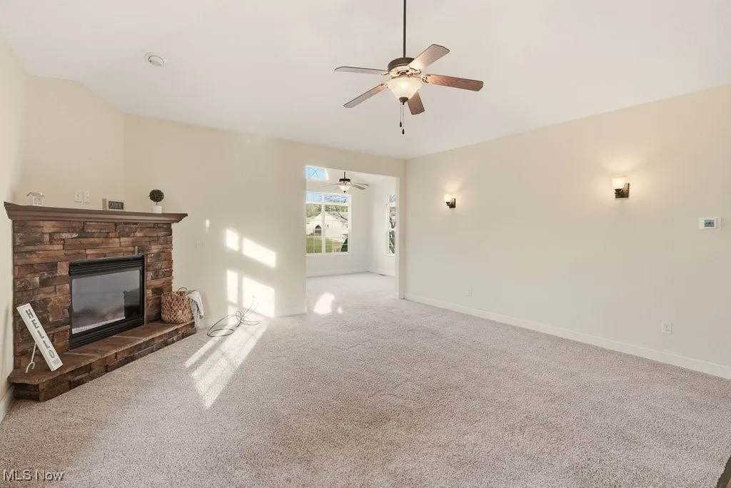 Unfurnished living room with carpet, a fireplace, vaulted ceiling, and ceiling fan
