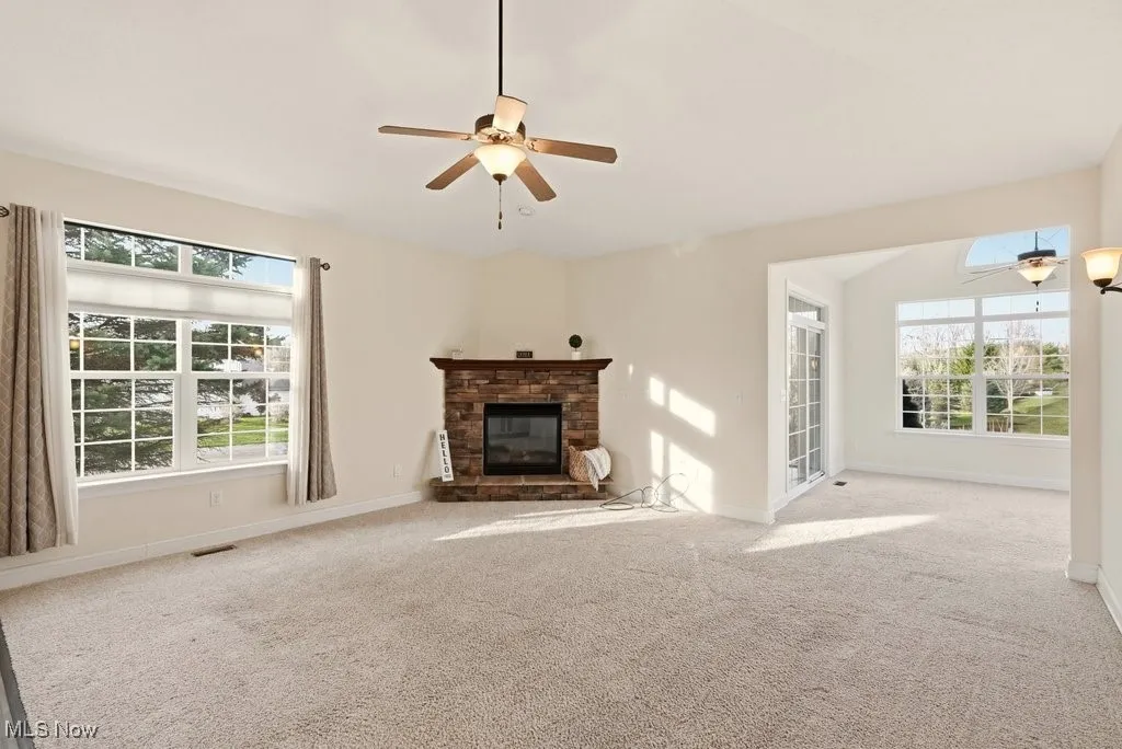 Unfurnished living room featuring a fireplace, light colored carpet, a ceiling fan, and healthy amount of natural light