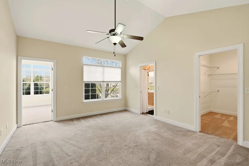 Primary bedroom featuring vaulted ceiling, light colored carpet, ensuite bathroom, a spacious walk in closet, access to sun room.