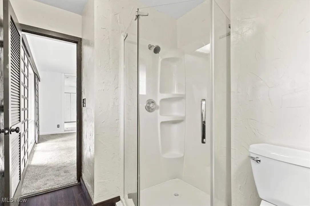 Full bathroom with a textured wall, a stall shower, and dark wood finished floors