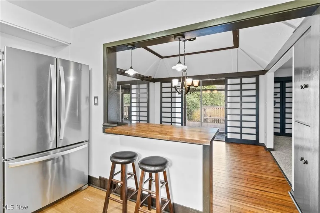 Kitchen with freestanding refrigerator, butcher block counters, hanging light fixtures, a kitchen breakfast bar, and light wood-type flooring
