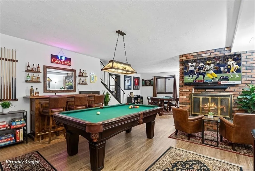 Rec room featuring a bar, wood finished floors, a textured ceiling, a brick fireplace, and pool table