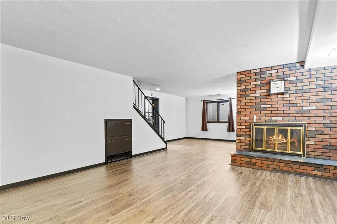 Unfurnished living room with a brick fireplace, stairway, light wood-style floors, and a textured ceiling
