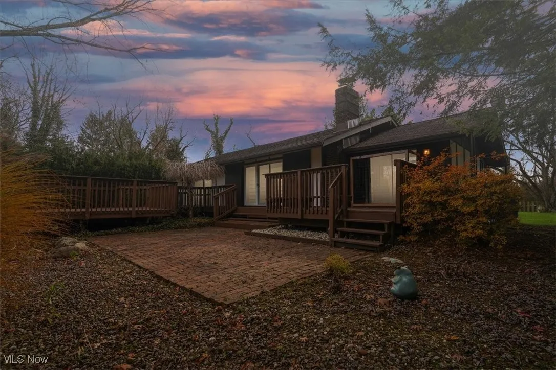 Back of property at dusk with a chimney and a deck