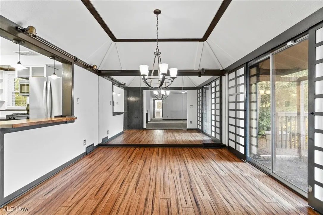 Unfurnished dining area featuring vaulted ceiling, wood-type flooring, and a chandelier