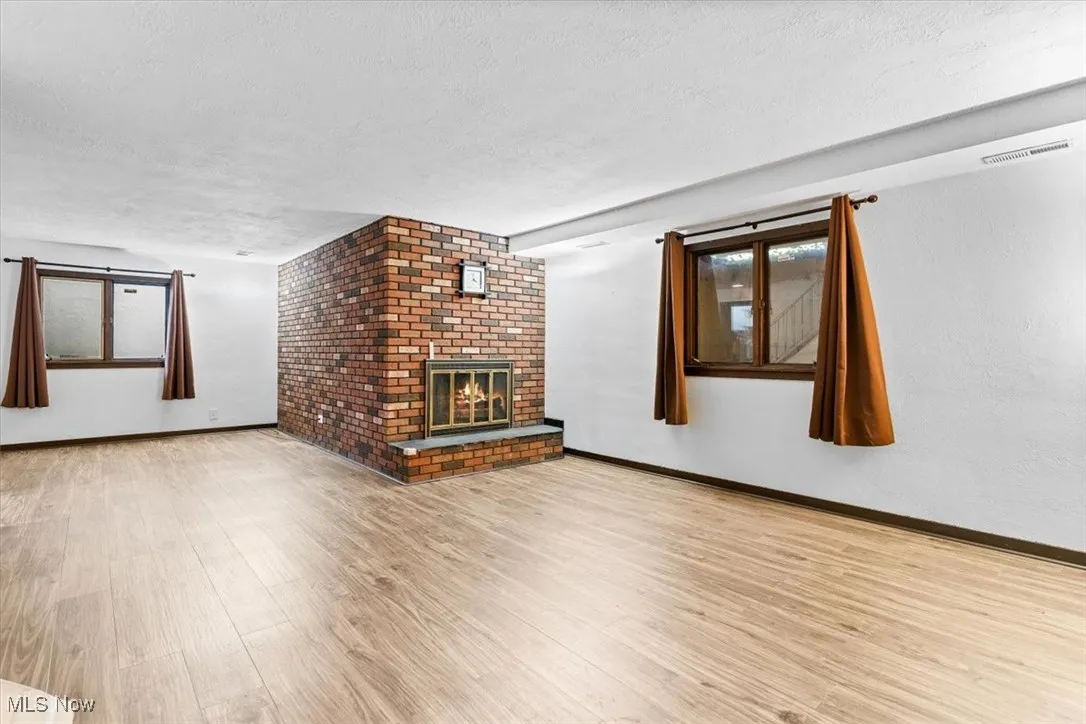 Unfurnished living room featuring a textured ceiling, wood finished floors, a brick fireplace, and plenty of natural light