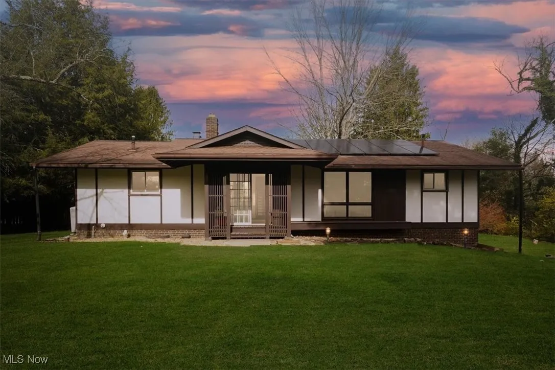 Back of property at dusk featuring roof mounted solar panels, a lawn, a chimney, and roof with shingles