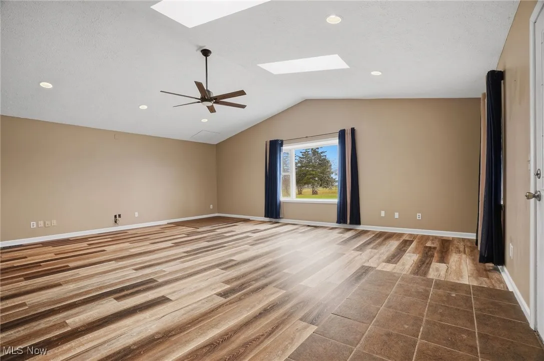 Empty room featuring a skylight, light wood-type flooring, lofted ceiling, a ceiling fan, and recessed lighting