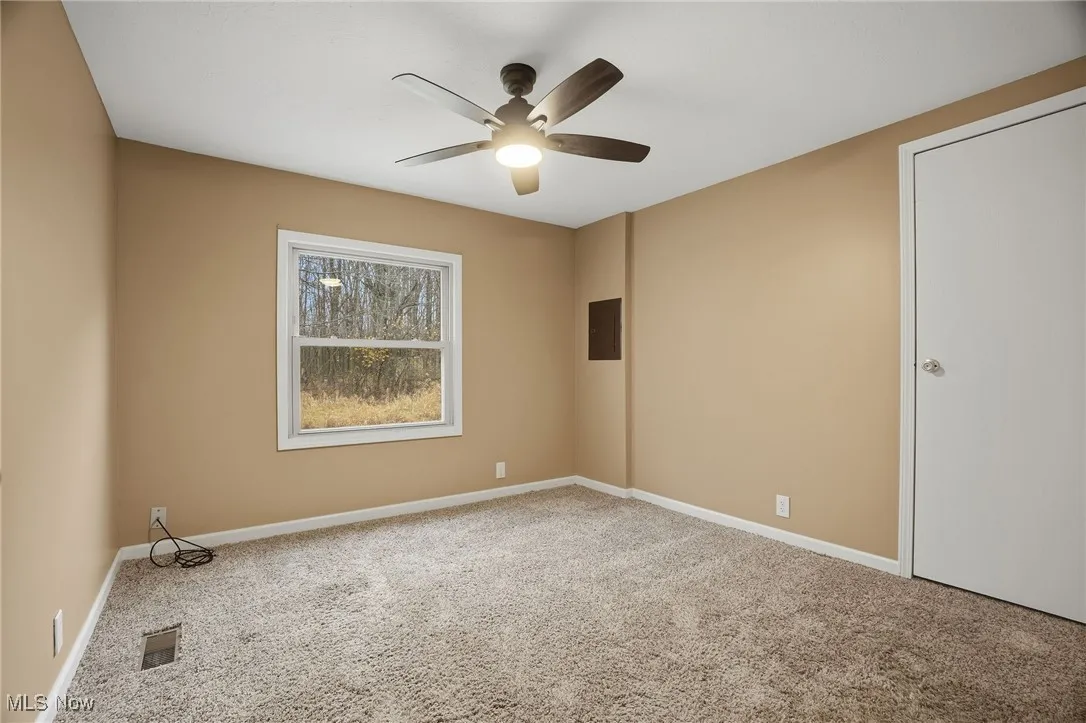 Carpeted empty room featuring electric panel and a ceiling fan