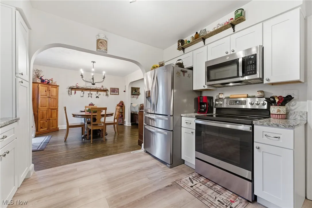Kitchen with stainless steel appliances, white cabinets, light stone countertops, and light wood-style floors