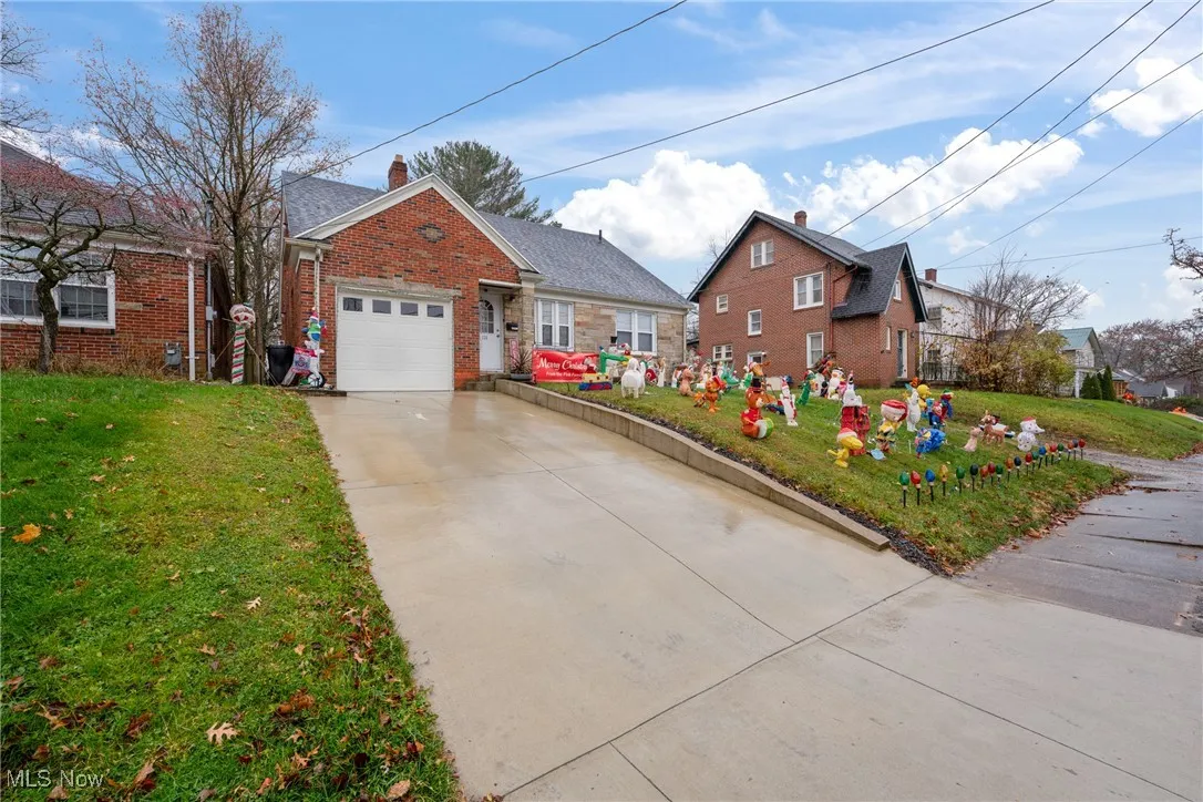 View of front facade featuring a front lawn, concrete driveway, a chimney, brick siding, and a garage