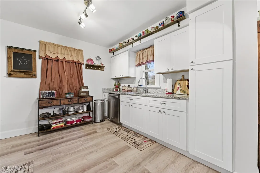 Kitchen featuring white cabinetry, light stone countertops, light wood-type flooring, and stainless steel dishwasher